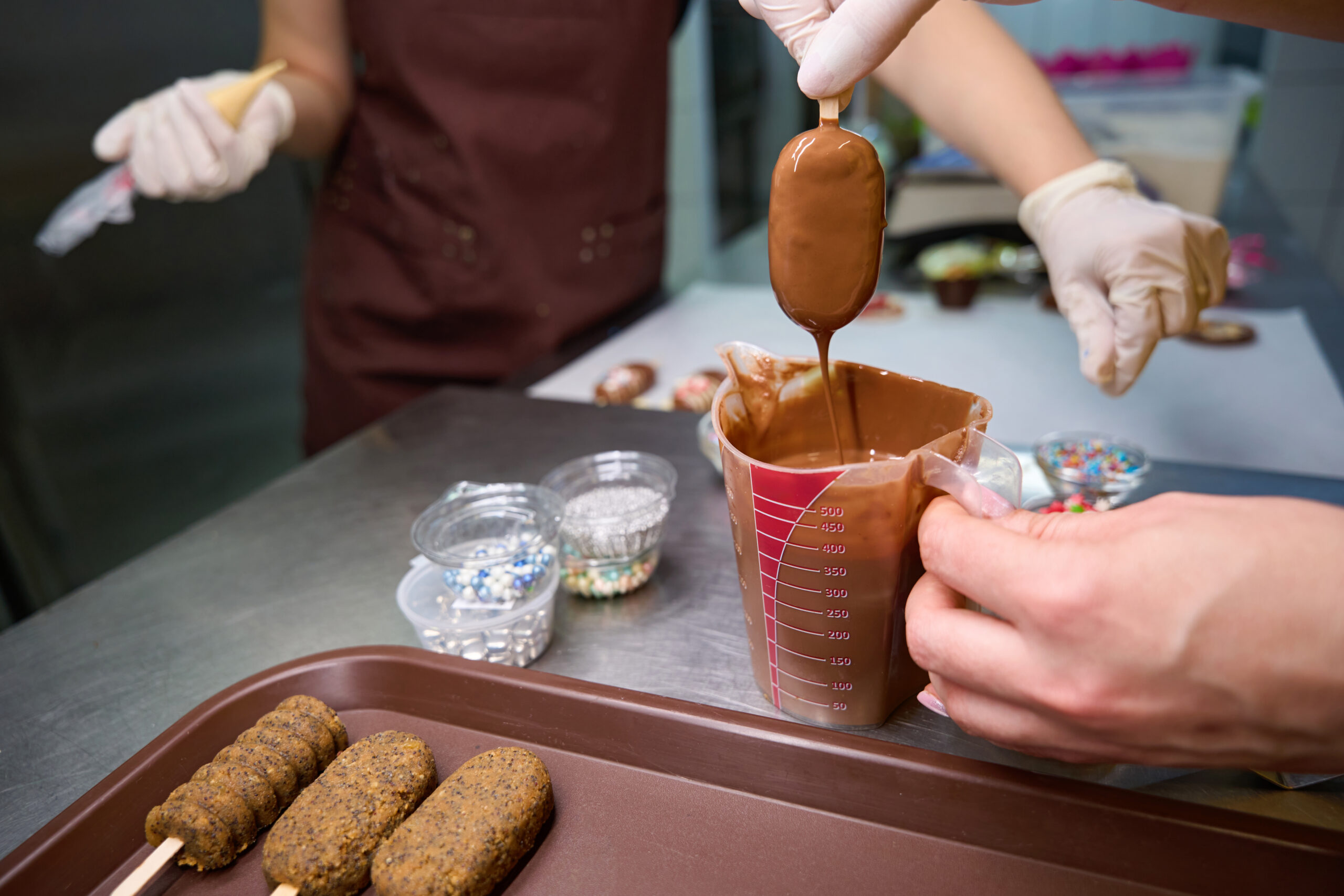 Confectioners making batch of cake popsicles on kitchen countertop